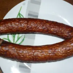 Okrągła, wędzona kiełbasa zwyczajna na talerzu z zielonym wzorem.