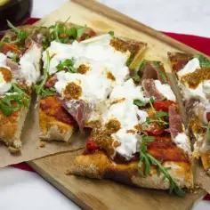 Pyszna pinsa z burratą, rukolą i szynką parmeńską, polana sosem.