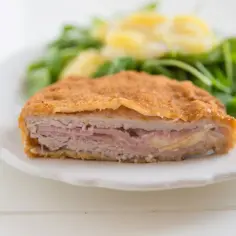 Schab po szwajcarsku, panierowany kotlet z szynką i serem, podany z sałatką.