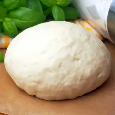 Świeże ciasto na pizzę z twarogu, gotowe do pieczenia, z bazylią w tle.