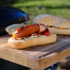 Pyszna kiełbasa z grilla w bułce z cebulą i papryką, gotowa do jedzenia na drewnianej desce.
