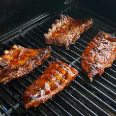 Soczyste żeberka w marynacie do żeberek skwierczą na grillu, nabierając apetycznego koloru.