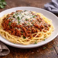 Pyszny sos do makaronu bolognese, posypany parmezanem i natką pietruszki, na białym talerzu.