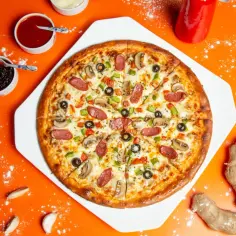 Pyszna pizza z kiełbasą, pieczarkami i papryką, obok sosy i imbir. Idealne dodatki do pizzy na pomarańczowym tle.