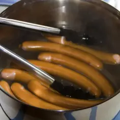 Parówki gotujące się w garnku z wodą, pokazujące, jak ugotować parówki. Szczypce pomagają je wyjąć.