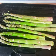 Zielone szparagi z parmezanem grillują się na czarnej patelni.