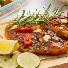 Karkówka w marynacie z chili, czosnkiem i rozmarynem, gotowa do grillowania. Obok cytryna i limonka.