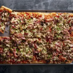 Oto najlepsza pizza przepis: prostokątna, obficie posypana pieczarkami, szynką i oliwkami, z ciągnącym się serem.