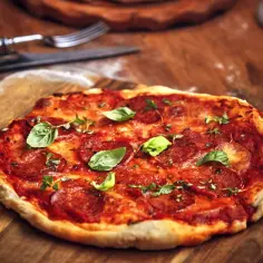 Pyszna pizza salami z bazylią i oregano, gotowa do podania na drewnianej desce.