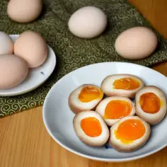 Na talerzu jajka do ramenu, połówki z płynnym, pomarańczowym żółtkiem. Obok całe jajka.