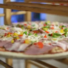 Surowa pizza z szynką, cebulą i kolorową papryką. Wszystkie składniki na pizzę ułożone na cieście, gotowe do pieczenia.