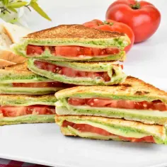 Stos pysznych, chrupiących kanapek z pomidorami i mozzarellą, polanych zielonym pesto. Ta włoska kanapka wygląda apetycznie!