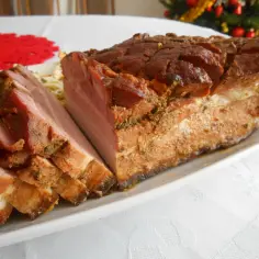Pieczony boczek pokrojony w plastry na białej talerzu, z widocznym fragmentem choinki w tle.