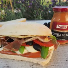 Pyszne panini z kurczakiem, mozzarellą, pomidorami, oliwkami i bazylią. Obok słoiczek musztardy pomidorowej Prymat.