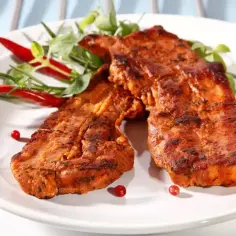 Dwa kawałki boczku na grilla, idealnie przyprawione marynatą do boczku na grilla, podane z papryczkami chili i zielonymi ziołami.
