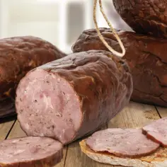 Kiełbasa żywiecka, wędzona, z widocznym przekrojem i plastrami na chlebie, prezentuje się apetycznie na drewnianym stole.