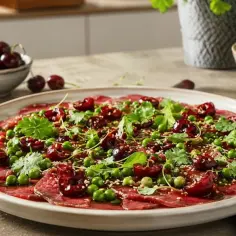 Eleganckie carpaccio wołowe z wiśniami, groszkiem i świeżą kolendrą, posypane sezamem.