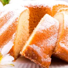 Puszysta, złocista babka z cukrem pudrem, pokrojona na kawałki. Wygląda na najbardziej wilgotna babka, jaką można sobie wymarzyć.