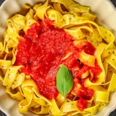 Pappardelle z sosem pomidorowym i listkiem bazylii. Różne rodzaje makaronu mogą mieć taką formę.