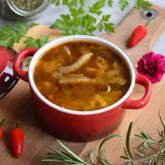 Aksamitne flaczki z boczniaków na rosole, podane w czerwonej miseczce, z dodatkiem papryczek chili i ziół.