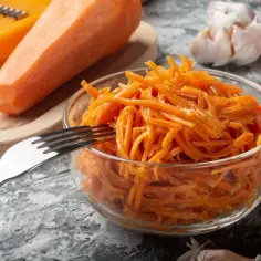 Pyszna surówka z marchewki jak z restauracji, gotowa do podania. Obok świeża marchewka, czosnek i papryczka chili.