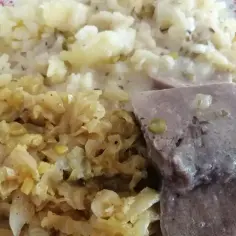 Na talerzu ułożone są plastry gotowanych ozorków w sosie, obok ziemniaki i duszona kapusta.