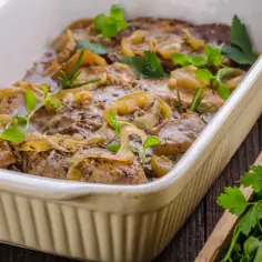 Soczysta łopatka pieczona w piekarniku, duszona z cebulą i ziołami, podana w białym naczyniu.