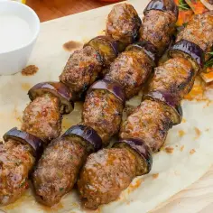 Kofta kebab z bakłażanem na desce, podany z sosem i pitą. Pyszne danie, które zachwyci każdego miłośnika kuchni bliskowschodniej.