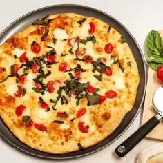 Pyszna pizza z serka wiejskiego, pomidorkami koktajlowymi i bazylią. Obok leży krajalnica do pizzy i świeże pomidory.
