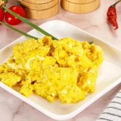 Puszysta jajecznica z serem, udekorowana szczypiorkiem, obok pomidorków i papryczki chili.