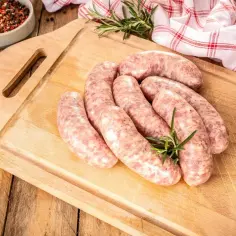 Surowa biała kiełbasa na desce, gotowa do parzenia. Obok przyprawy i czosnek.