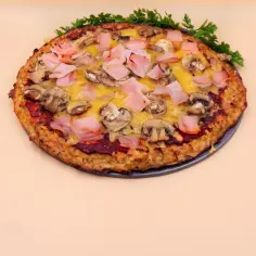 Pizza z kalafiora z szynką i pieczarkami, ozdobiona natką pietruszki.