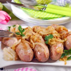Pyszna biała kiełbasa surowa pieczona w piekarniku z cebulą, podana na talerzu z natką pietruszki.