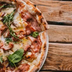 Pyszna pizza carbonara z chrupiącym boczkiem, rukolą i cebulą na drewnianym blacie.