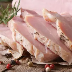 Pokrojony, super delikatny i soczysty schab gotowany, przyprawiony pieprzem, z gałązką rozmarynu na drewnianym blacie.