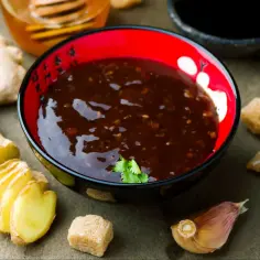 Sos teriyaki przepis: aromatyczny sos w miseczce, obok świeży imbir, czosnek i cukier. Idealny do dań kuchni azjatyckiej.