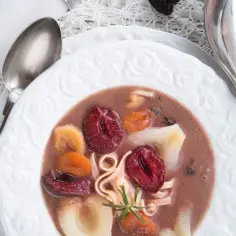 Zupa z krwi, czyli słodka zupa owocowa z suszonymi śliwkami, morelami i makaronem, podana w białej misce.