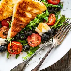 Najlepsza sałatka z halloumi: grillowany ser, pomidorki, oliwki i rukola na białym talerzu, gotowa do podania.