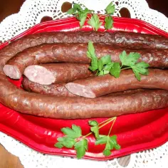 Gotowa do wędzenia kiełbasa na czerwonej tacy, ozdobiona natką pietruszki. Idealny przykład, jak wędzić kiełbasę.