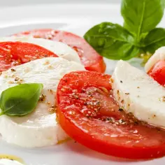 Pyszna mozzarella z pomidorami, skropiona oliwą i posypana pieprzem, ozdobiona listkami bazylii.