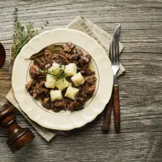 Miękka wątróbka wieprzowa z ziemniakami na talerzu, obok szklanka z napojem i młynek do pieprzu. Idealny sposób, jak zrobić wątróbkę wieprzową żeby była miękka.
