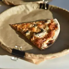 Kawałek pizzy z pieczarkami na brązowym papierze. Zastanawiasz się, ile kcal ma kawałek pizzy?