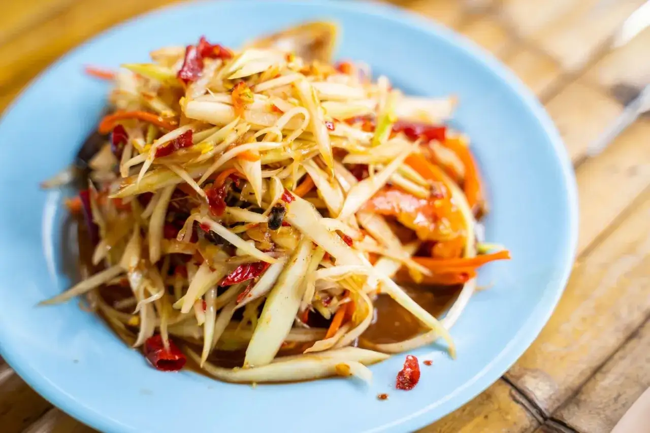 Pikantna surówka jak u chińczyka z zielonej papai, marchewki i chili na jasnoniebieskim talerzu.