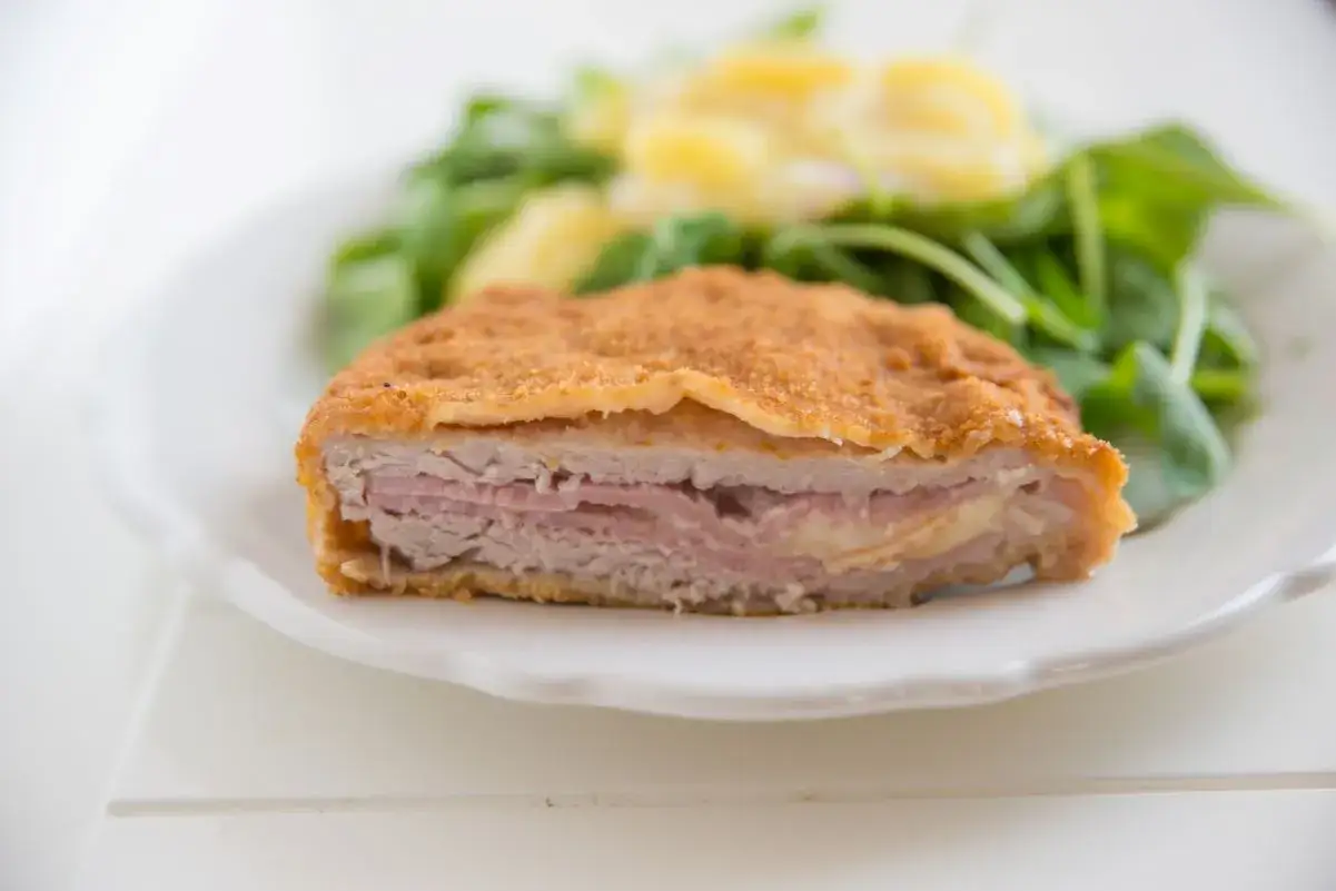 Schab po szwajcarsku, panierowany kotlet z szynką i serem, podany z sałatką.