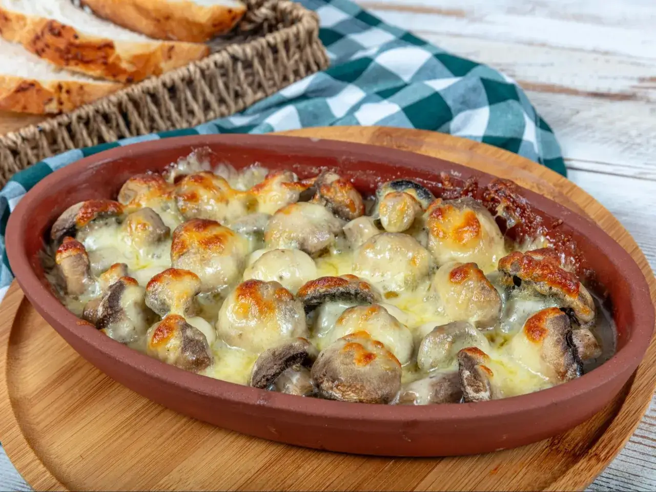 Pyszne pieczarki z piekarnika zapieczone pod ciągnącym serem w glinianym naczyniu, obok koszyk z chlebem.
