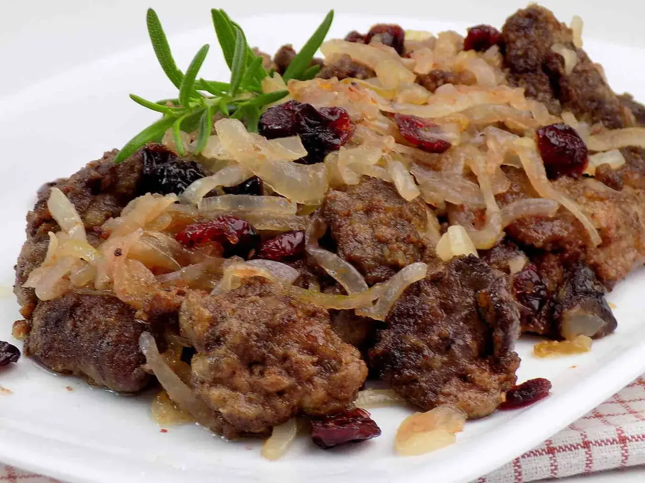Pyszna wątróbka drobiowa duszona z cebulką i żurawiną, udekorowana gałązką rozmarynu.