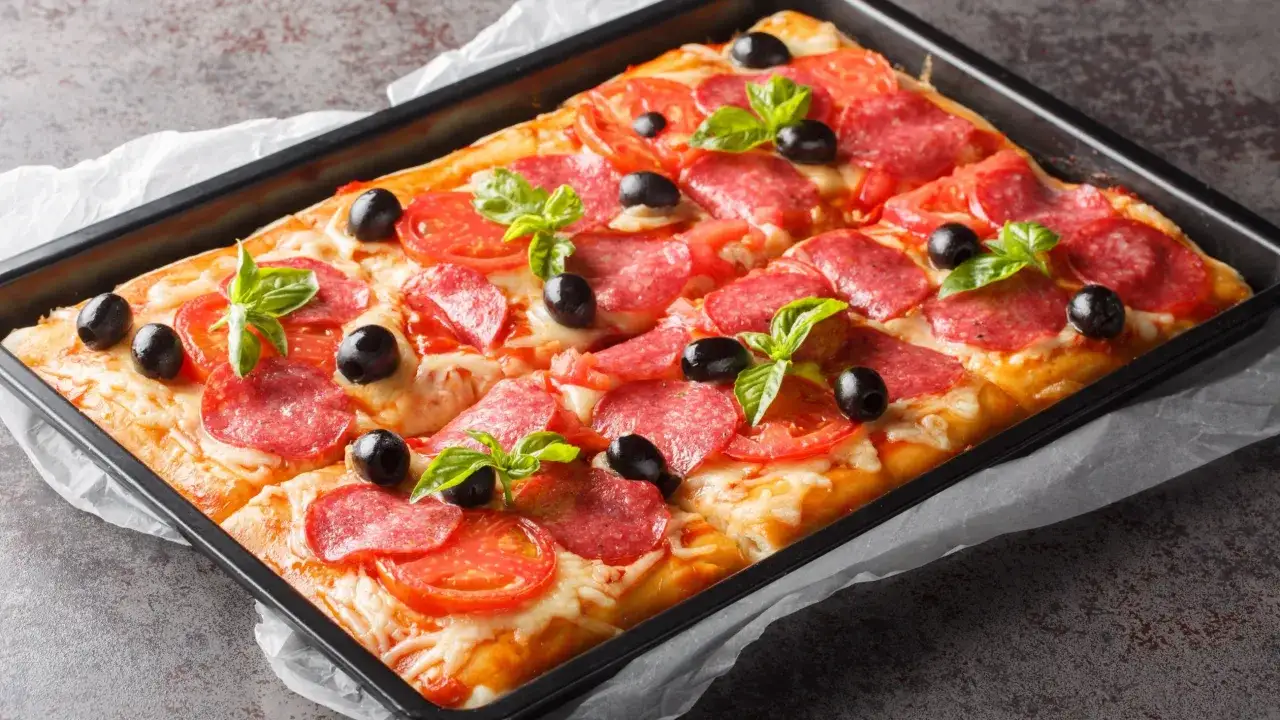 Prostokątna pizza z salami, pomidorami i oliwkami, ozdobiona bazylią. Idealna na rodzinne spotkanie, bo ile piec pizze, tyle radości!
