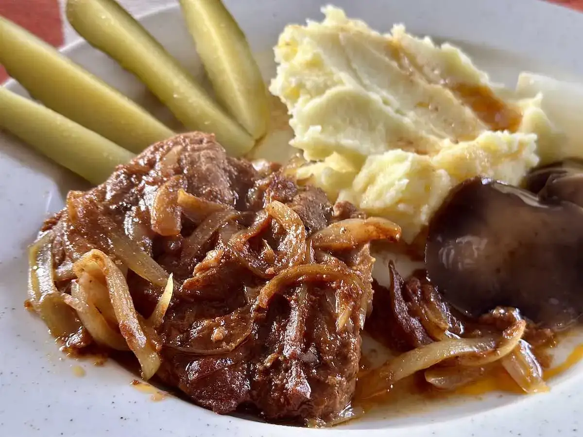 Kotlety z karkówki duszone z cebulką, podane z puree ziemniaczanym, ogórkami konserwowymi i grzybem.
