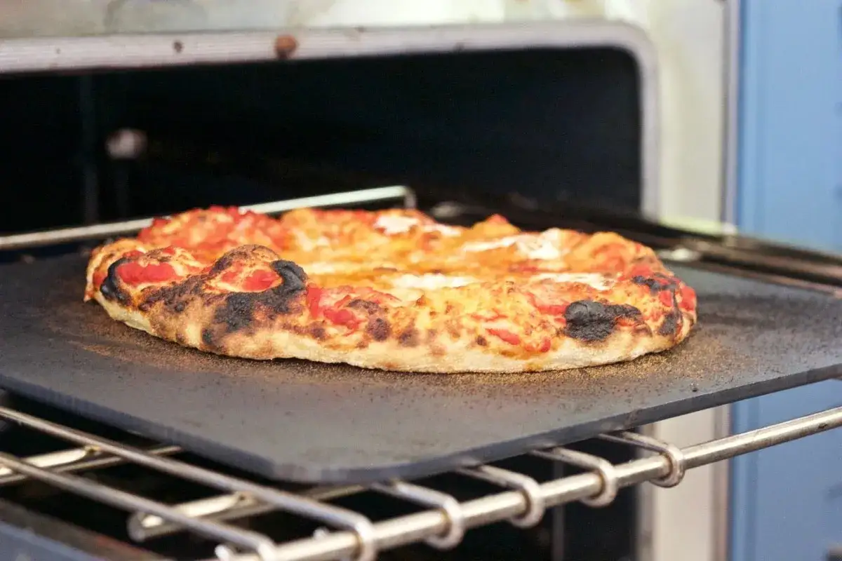 Pieczenie pizzy w wysokiej temperaturze, ok. 250°C, daje taki efekt. Ciasto jest chrupiące, a brzegi lekko przypalone.