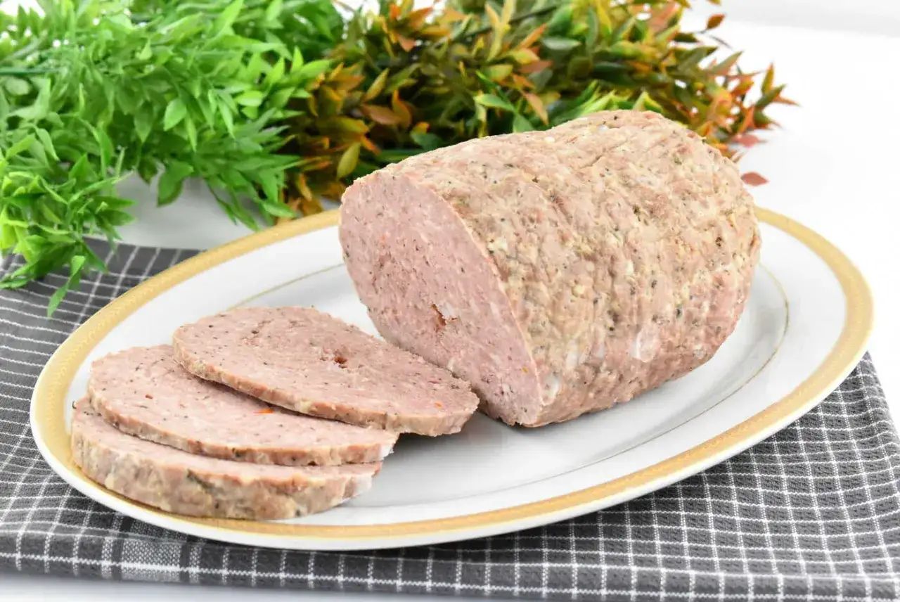 Pokrojona mielonka tyrolska na talerzu, obok zielone liście.